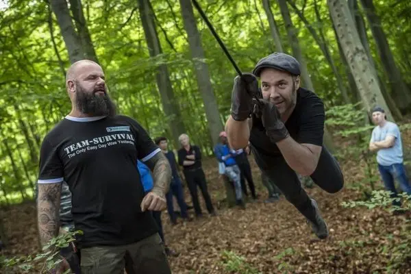 Ein Teilnehmer schwingt an einem Seil durch den Wald, während andere zuschauen