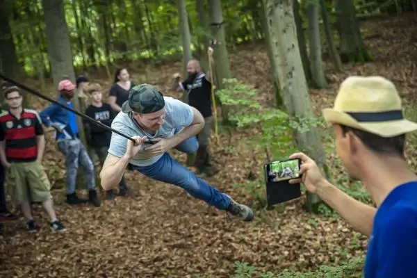 Ein Teilnehmer schwingt an einer Seilbrücke durch den Wald, während andere zuschauen