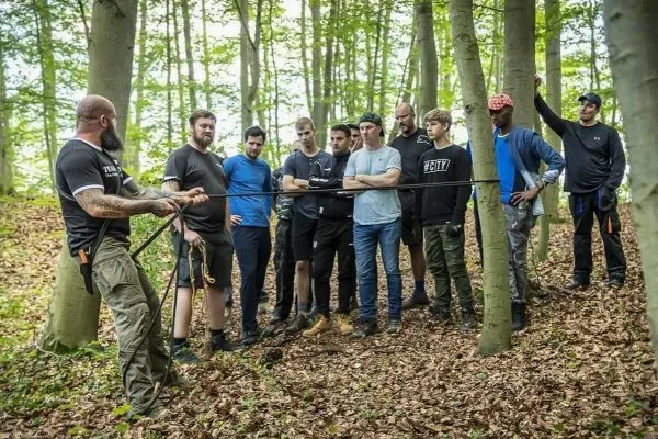 Ein Trainer demonstriert eine Seiltechnik vor einer Gruppe im Wald
