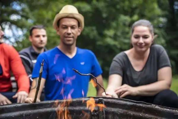 Feuer brennt in einem Metallbehälter, während Personen mit Stöcken daneben sitzen