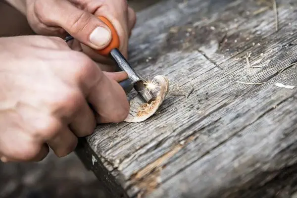 Feuerstahl erzeugt Funken auf Zunderstück auf Holzoberfläche