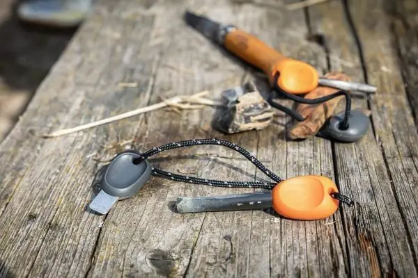 Feuerstahl und Messer liegen auf einer Holzoberfläche neben Zunder