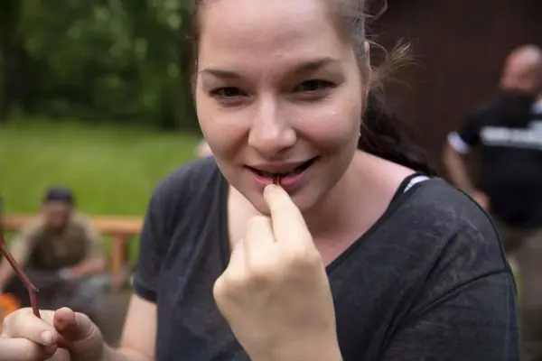 Frau hält einen kleinen Gegenstand zwischen den Fingern und schaut lächelnd in die Kamera