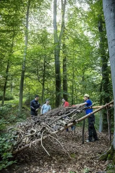 Gruppe baut eine Laubhütte aus Ästen und Zweigen im Wald