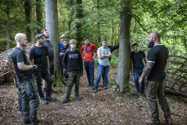 Gruppe hört einem Trainer im Wald aufmerksam zu