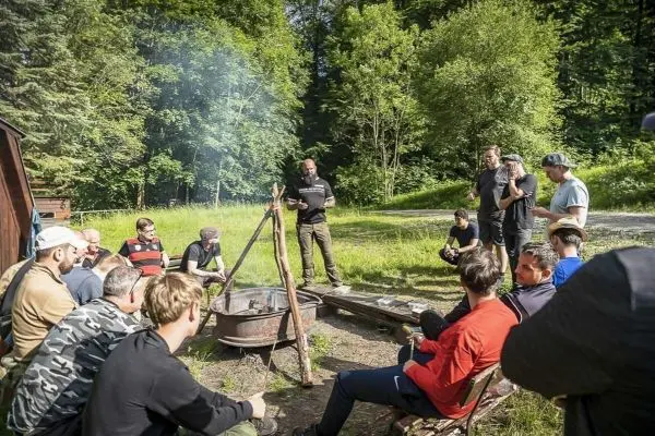 Gruppe sitzt um ein Feuer, während ein Mann Anweisungen gibt