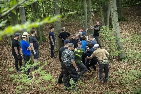 Gruppe übt Knotentechniken mit Seil zwischen Bäumen im Wald