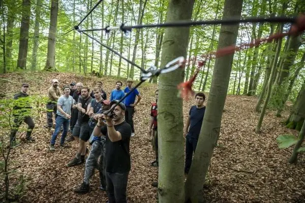 Gruppe von Personen beobachtet eine selbstgebaute Seilbrücke im Wald