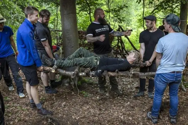 Gruppe von Personen hebt eine selbstgebaute Trage im Wald