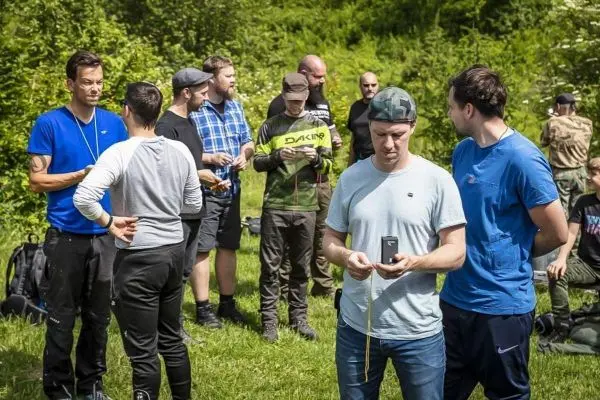 Gruppe von Personen in Outdoor-Bekleidung steht auf einer Wiese und kommuniziert