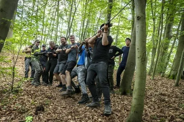 Gruppe zieht an einem Seil in einem Waldgebiet mit Laubboden