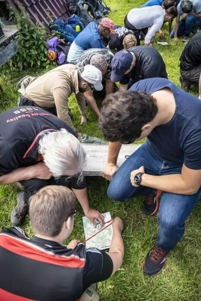 Gruppenteilnehmer betrachten eine Karte auf einer Holzbank beim Überlebenstraining