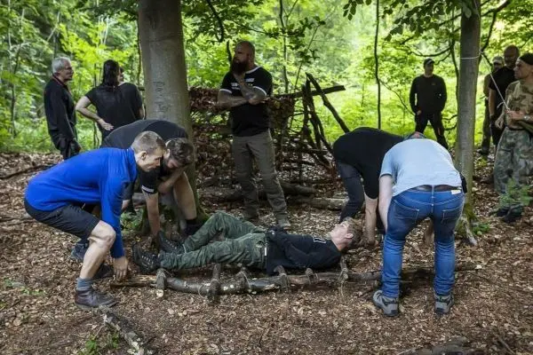 Gruppierung von Personen hebt eine improvisierte Trage aus Ästen an