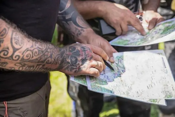 Hände mit Karten und Tätowierungen zeigen auf geografische Merkmale