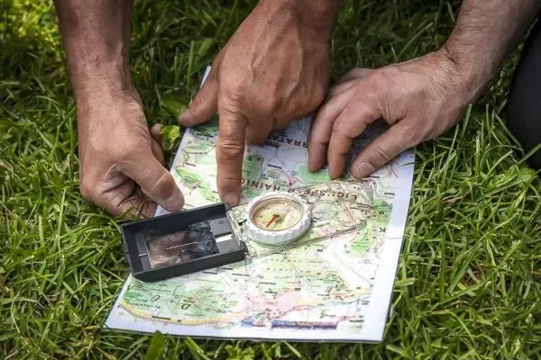 Hände zeigen auf eine Karte und einen Kompass im Gras beim Orientieren