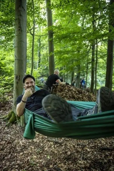 Hängematte zwischen Bäumen mit Person, die entspannt sitzt und lächelt