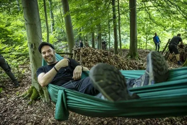 Hängematte zwischen Bäumen, Person entspannt mit Lächeln, Laub im Hintergrund