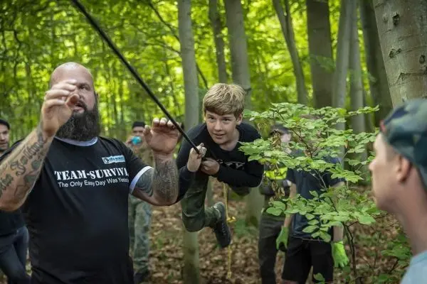 Junge schwingt an einem Seil über den Boden, während Erwachsene anleiten