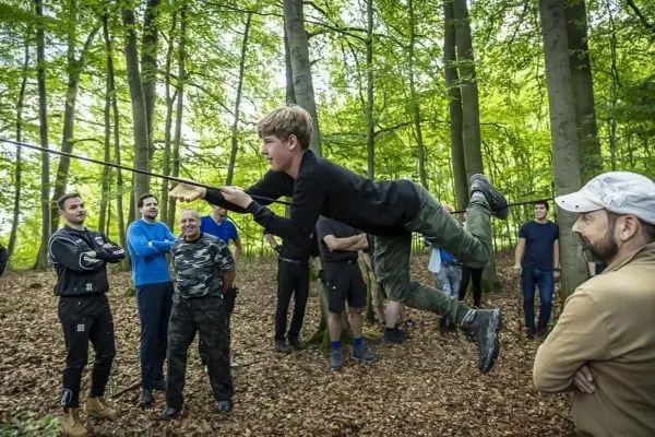 Junge schwingt an einer Seilbrücke über den Boden, Zuschauer beobachten