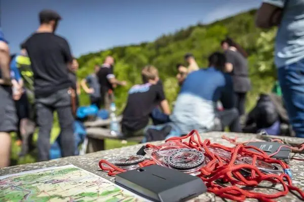 Karte und Kompasse liegen auf einem Tisch, während Gruppenaktivität im Hintergrund stattfindet