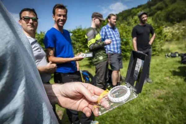Kompass wird in der Hand gehalten, während Teilnehmer im Hintergrund stehen