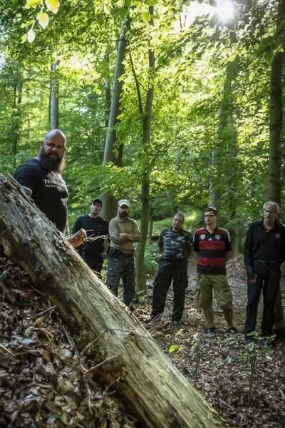 Mann demonstriert Technik an umgefallenem Baumstamm, Gruppe beobachtet aufmerksam
