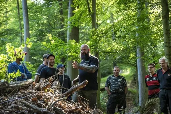 Mann erklärt Techniken zur Holzverarbeitung vor einer Gruppe im Wald