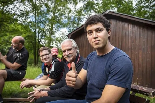 Mann gibt Daumen hoch, während andere im Hintergrund sitzen und sich unterhalten