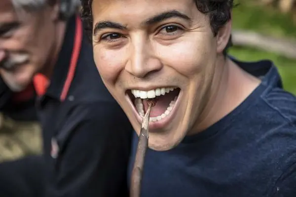 Mann hält einen Stock im Mund und lächelt in die Kamera