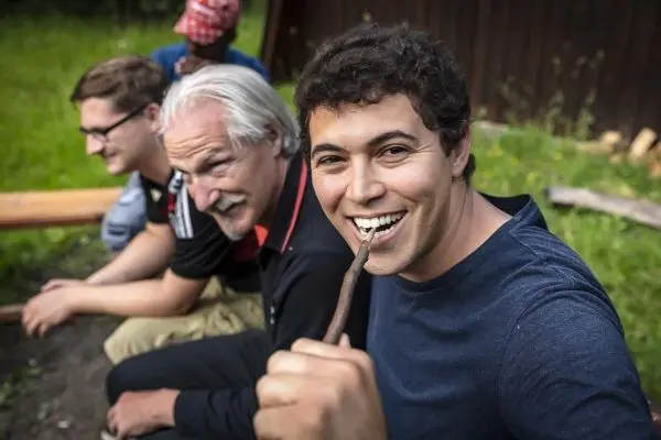 Mann hält einen Stock im Mund und lächelt in die Kamera