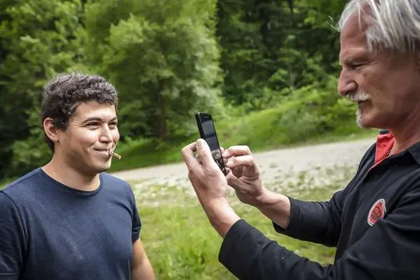 Mann hält Smartphone und fotografiert lächelnden Mann mit Zunder im Mund