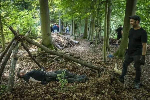 Mann liegt unter einer improvisierten Notunterkunft aus Ästen im Wald