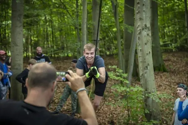 Mann schwingt an einem Seil zwischen Bäumen und lächelt dabei