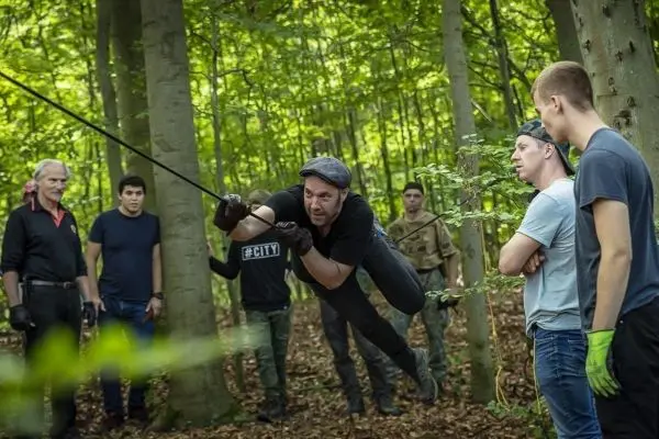 Mann schwingt an einem Seil zwischen Bäumen, Zuschauer beobachten aufmerksam