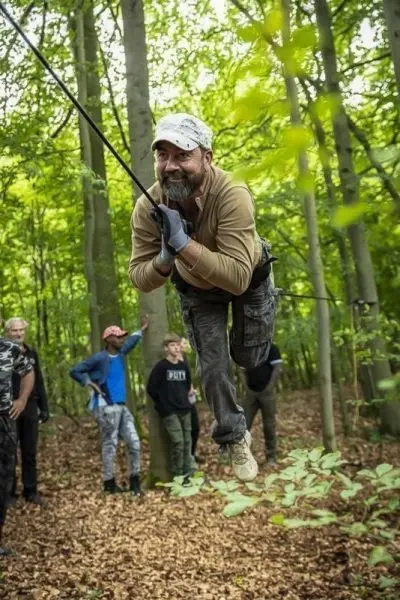 Mann schwingt an einer Seilbrücke zwischen Bäumen im Wald