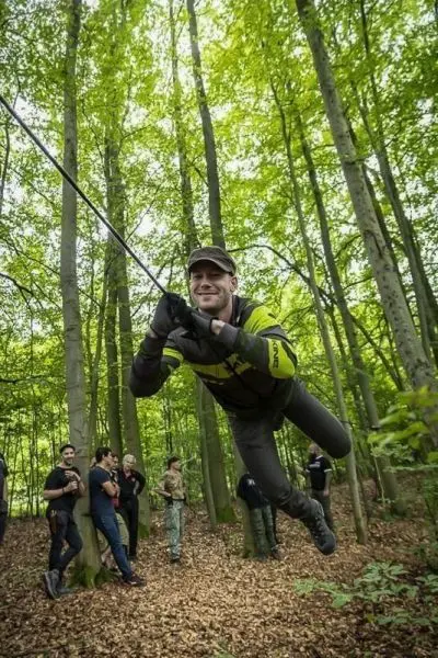 Mann schwingt an einer Seilbrücke zwischen Bäumen im Wald