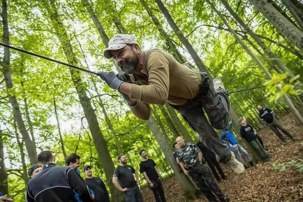 Mann schwingt an einer Seilbrücke zwischen Bäumen über einer Gruppe von Zuschauern