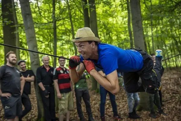 Mann schwingt an Seil durch den Wald, Zuschauer beobachten gespannt