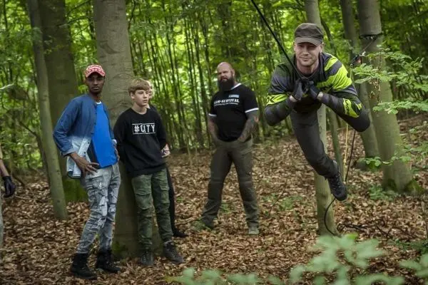 Mann schwingt an Seil zwischen Bäumen, während andere zuschauen