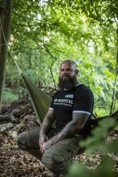Mann sitzt in einer Hängematte zwischen Bäumen im Wald