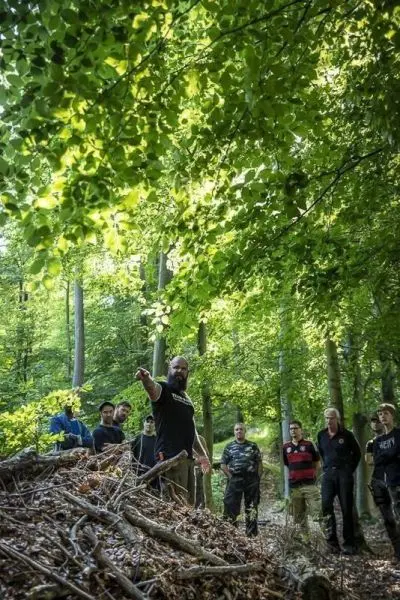 Mann zeigt auf einen Haufen aus Ästen und Laub im Wald