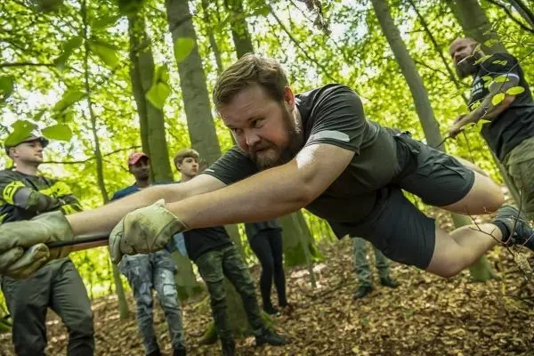 Mann zieht an einem Seil in einem Wald, während andere zuschauen