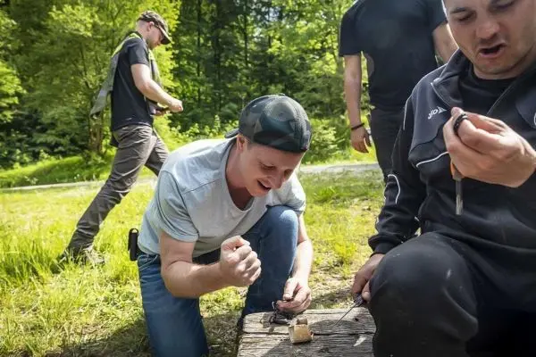 Mann zündet Zunder mit Feuerstahl auf Holzunterlage an