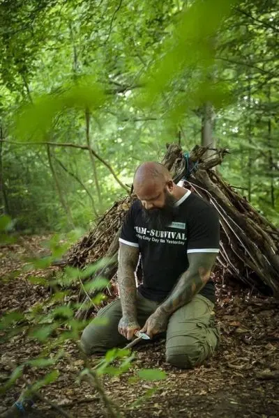 Messer schneidet Holzstücke vor einer selbstgebauten Laubhütte im Wald