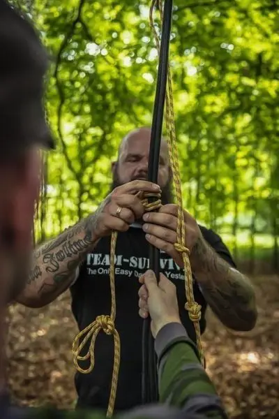 Person befestigt Seil an einem Stock im Wald