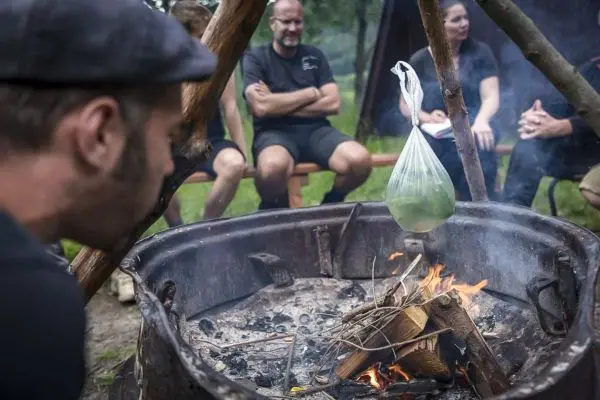 Person beobachtet einen über dem Feuer hängenden Beutel beim Kochen