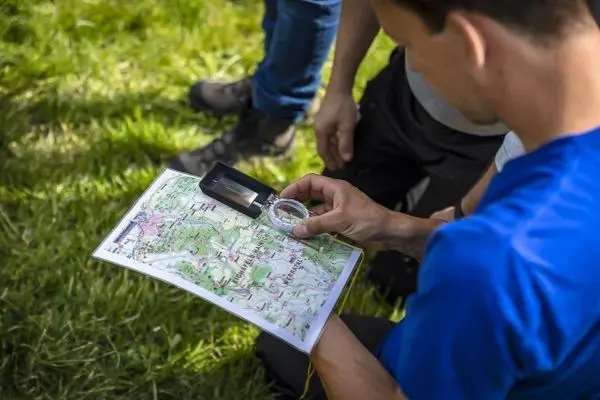 Person betrachtet eine Karte mit einem Kompass im Gras