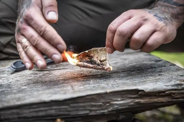 Person entzündet Papier auf einem Holzstück beim Survival Training