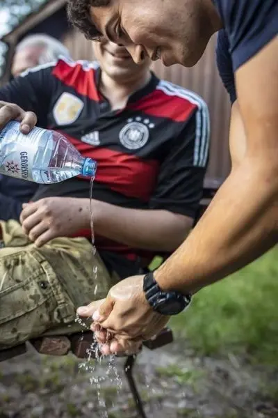 Person gießt Wasser aus einer Flasche über die Hände einer anderen Person