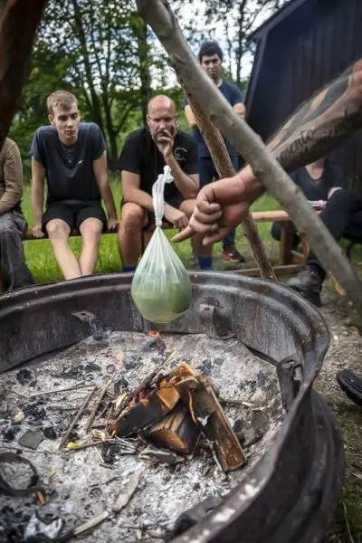 Person hält einen Beutel über ein Feuer beim Survival Training
